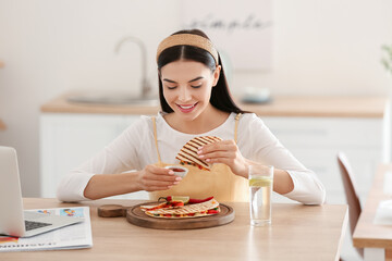 Canvas Print - Beautiful young woman eating tasty quesadilla at home