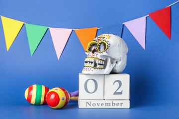 Painted human skull for Mexico's Day of the Dead (El Dia de Muertos), calendar, maracas and garland on color background