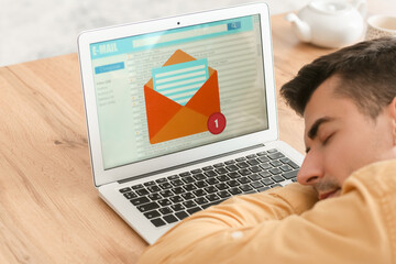 Laptop with open e-mail box and young man sleeping at table