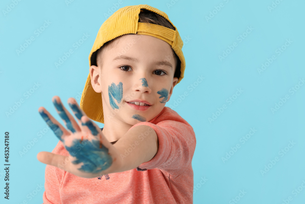 Little boy with hand and face in paint on color background