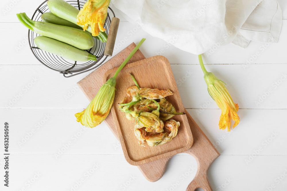 Board with fried zucchini flowers on light wooden background