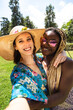 Smiling and happy young multiracial female couple take selfie in the park in summertime. Vertical image.
