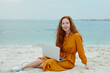© PinkCoffee Studio - Young beautiful woman sitting and working on the beach with lap top.