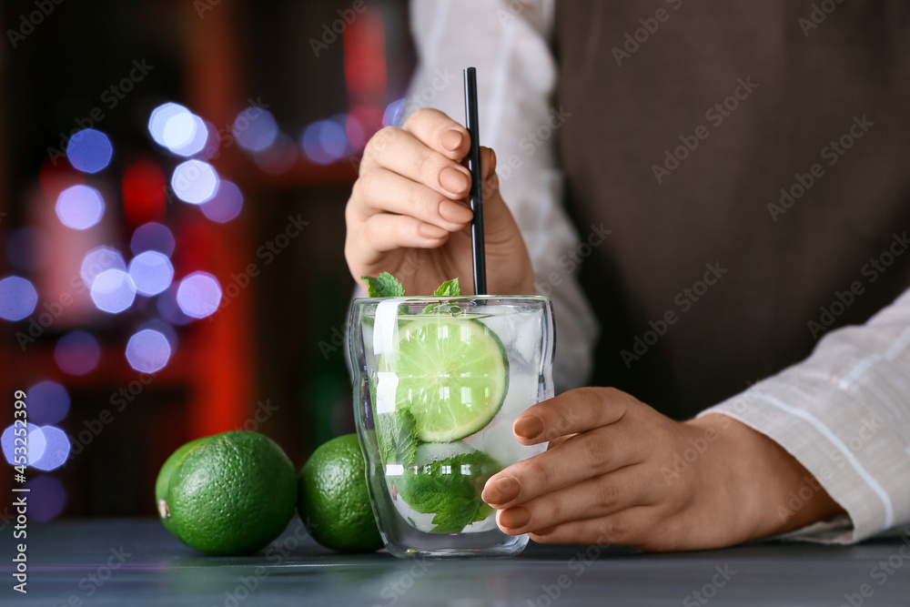 Female bartender with glass of fresh mojito  on table in bar