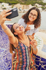 Wall Mural - Two young spanish cheerful women taking selfies eating ice cream