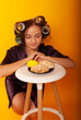 © Marina Chernivetskay - a girl in curlers looks at croissans a housewife cooked homemade cakes on a yellow isolated background