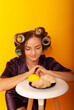 © Marina Chernivetskay - a girl in curlers looks at croissans a housewife cooked homemade cakes on a yellow isolated background