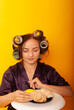 © Marina Chernivetskay - a girl in curlers looks at croissans a housewife cooked homemade cakes on a yellow isolated background