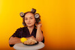 © Marina Chernivetskay - a girl in curlers looks at croissans a housewife cooked homemade cakes on a yellow isolated background
