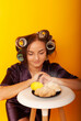 © Marina Chernivetskay - a girl in curlers looks at croissans a housewife cooked homemade cakes on a yellow isolated background