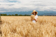 © Yelena Belodedova - a young attractive woman in a white dress and a straw hat on a field of ripe cereals against a blue sky with clouds in autumn, the concept of harvesting, agribusiness and agriculture