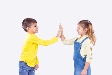 Two adorable brother and sister give high five agree to work as team, standing sideways and smiling.