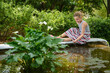 Teen girl is sitting near decorative garden pond