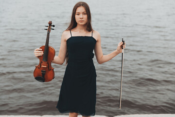 Poster - a beautiful girl with a violin stands against the background of water. Asian appearance. musical concept