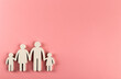 Wooden figurines of family on pink paper background.