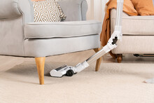 Cleaning Home Carpet In Interior Under Armchair With Wireless Vacuum Cleaner. Close-up Of Vacuum Cleaner Brush.