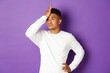Image of annoyed and bothered african-american male student, slap forehead, making facepalm and rolling eyes from something stupid, standing over purple background