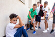 Group of schoolboys bullying a sad and upset looking boy.