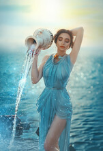 Art Photo Portrait Mythical Girl Greek Goddess. Astrological Sign Zodiac Aquarius. Fantasy Woman Pours Water From Clay Jug. Blue Chiffon Old Vintage Long Silk Dress. Fabulous Lake Magical Light Sunset