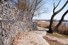 A Wall Of Stones On The River Embankment. Fencing Made Of Stone And Wire Mesh. Stones In A Wire Mesh. Fencing Made Of Natural Materials. The Mesh Holds Stones Back.