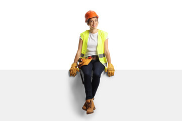 Full length portrait of a female construction worker sitting on a blank panel