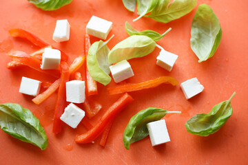 mozzarella and pepper. Close-up chopped pepper, white cheese and basil on an orange background. Flat lay top-down. Cubes of cheddar cheese isolated on red