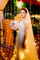 Wall Mural - bride with bouquet of flowers in night park against background of garland.