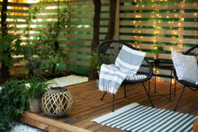 Exterior Veranda Of House With Black Acapulco Armchairs And Plants Pots. Cozy Space In Patio Or Balcony With Garland. Interior Wooden Verande With Garden Furniture. Modern Lounge Outdoors In Backyard