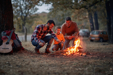 Wall Mural - Father, son and grandson enjoying a campfire in the forest