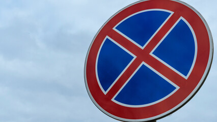 Round road sign with a red cross on a blue background. A sign means a parking prohibition. Dramatic sky background. Space for text.