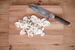 Sliced white mushrooms on a wooden cutting board.