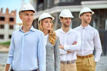 Wall Mural - Four adult people in hardhats standing on the building site