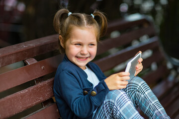 a little girl in a school uniform, sitting on a bench, and holding a tablet in her hands