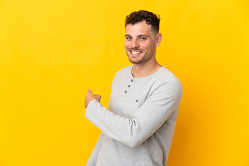 Young caucasian handsome man isolated on yellow background pointing back