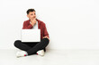 © luismolinero - Young handsome caucasian man sit-in on the floor with laptop having doubts and with confuse face expression