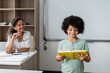 smiling african american teacher looking at schoolboy reading book in classroom