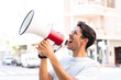 © luismolinero - Young caucasian man at outdoors shouting through a megaphone to announce something in lateral position