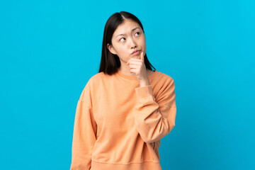 Wall Mural - Young Chinese girl over isolated blue background having doubts