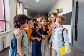 Wall Mural - cheerful multicultural kids talking and hugging in school hall