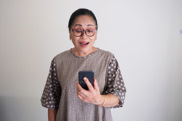 Wall Mural - Elderly Asian woman with shocked face expression while looking to her mobile phone