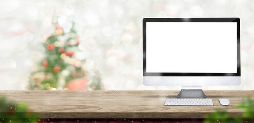 Poster - Merry Christmas with blank desktop computer on wood table at blur bokeh xmas tree decor with string light background,Winter banner backdrop for holiday greeting card advertise promotion on online