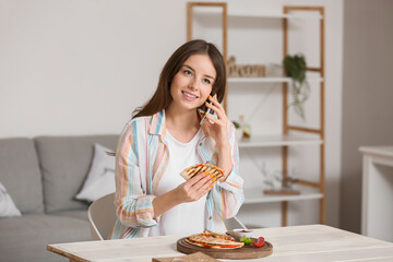 Canvas Print - Beautiful young woman eating tasty quesadilla while talking by phone at home