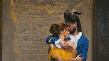 Enchanted Fairy Prince In Love, Man Gently Hugs Beautiful Cute Fantasy Woman. King Head Decorated Decorative Ram Horns. Vintage Retro Theatrical Carnival Costumes. Backdrop Loft Brick Wall