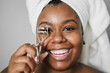 Black girl using eyelash curler while wearing body towel - Main focus on eyes