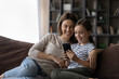 © fizkes - Affectionate young mother using cellphone applications with joyful little preteen child daughter, playing games, enjoying spending time online watching funny photo video content in social networks.
