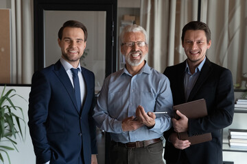 Wall Mural - Portrait of three smiling confident businessmen employees startup team with mature executive standing in office, businesspeople workers coworkers group looking at camera, posing for corporate photo