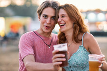 A Tipsy Couple Is Standing Outdoor At A Music Festival And Goofing Around.