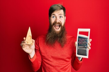 Wall Mural - Redhead man with long beard holding grater and cheese celebrating crazy and amazed for success with open eyes screaming excited.