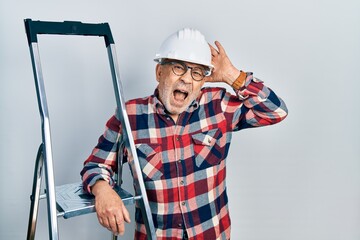 Canvas Print - Handsome mature handyman close to construction stairs wearing hardhat crazy and scared with hands on head, afraid and surprised of shock with open mouth