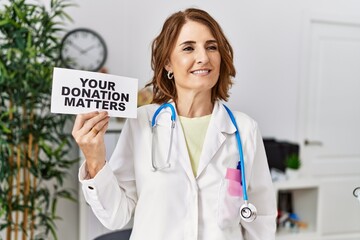 Canvas Print - Middle age doctor woman holding your donation matters at the clinic looking positive and happy standing and smiling with a confident smile showing teeth